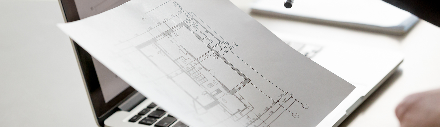 A floorplan held by a person in front of a laptop