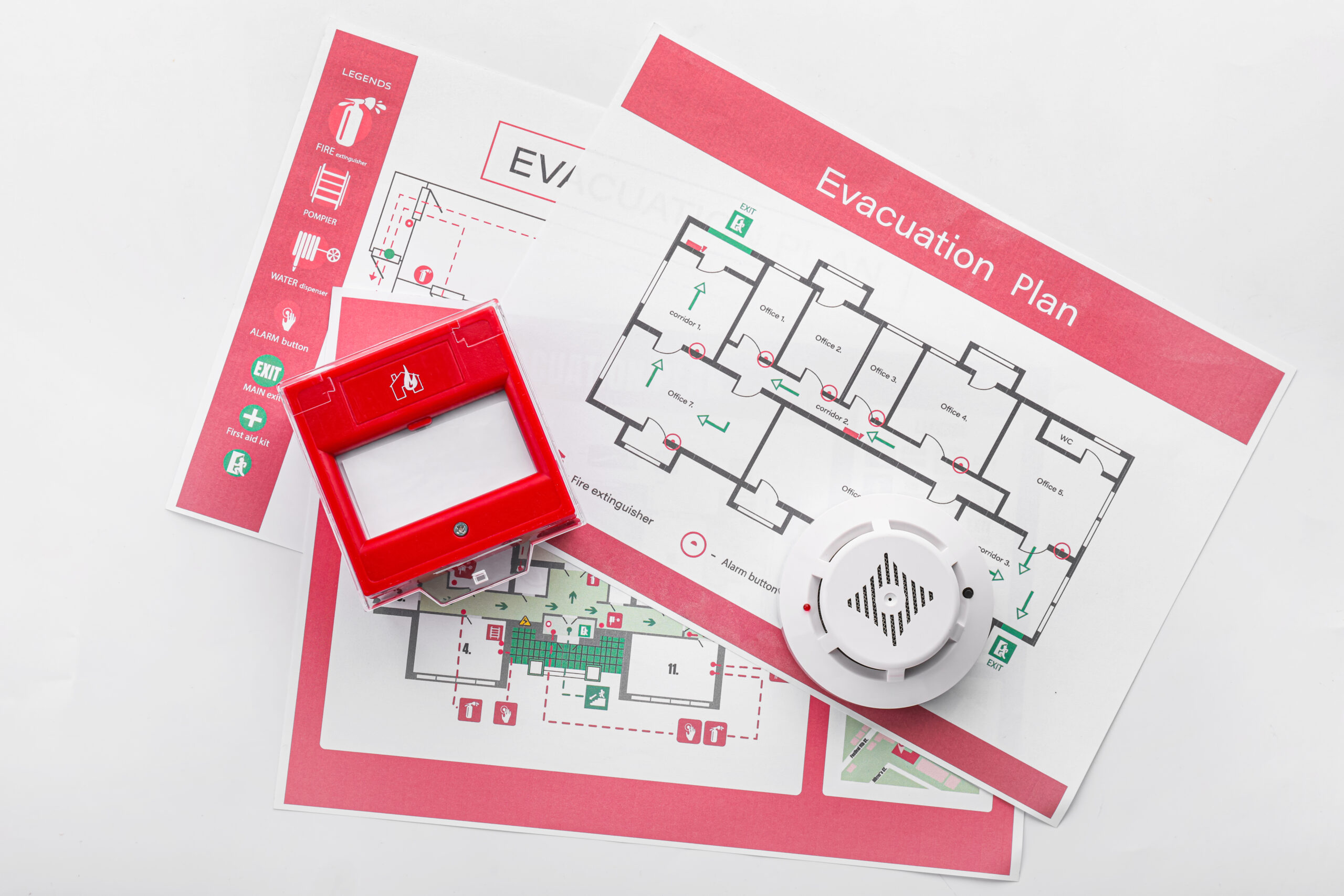 A fire evacuation plan with a fire alarm and smoke detector on top of the plans